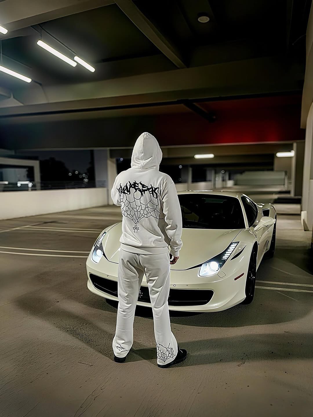 Person in white standing in front of a white sports car at night