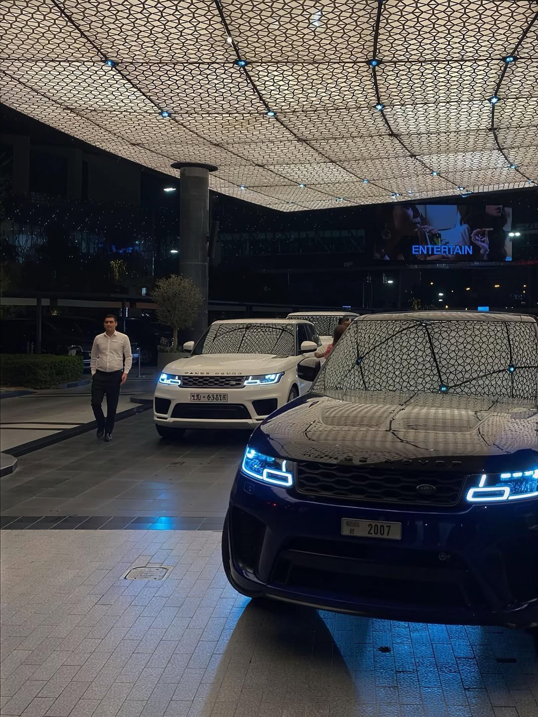 Two luxury SUVs arriving beneath an illuminated entrance canopy